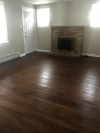 an empty room with wooden floor fireplace and windows