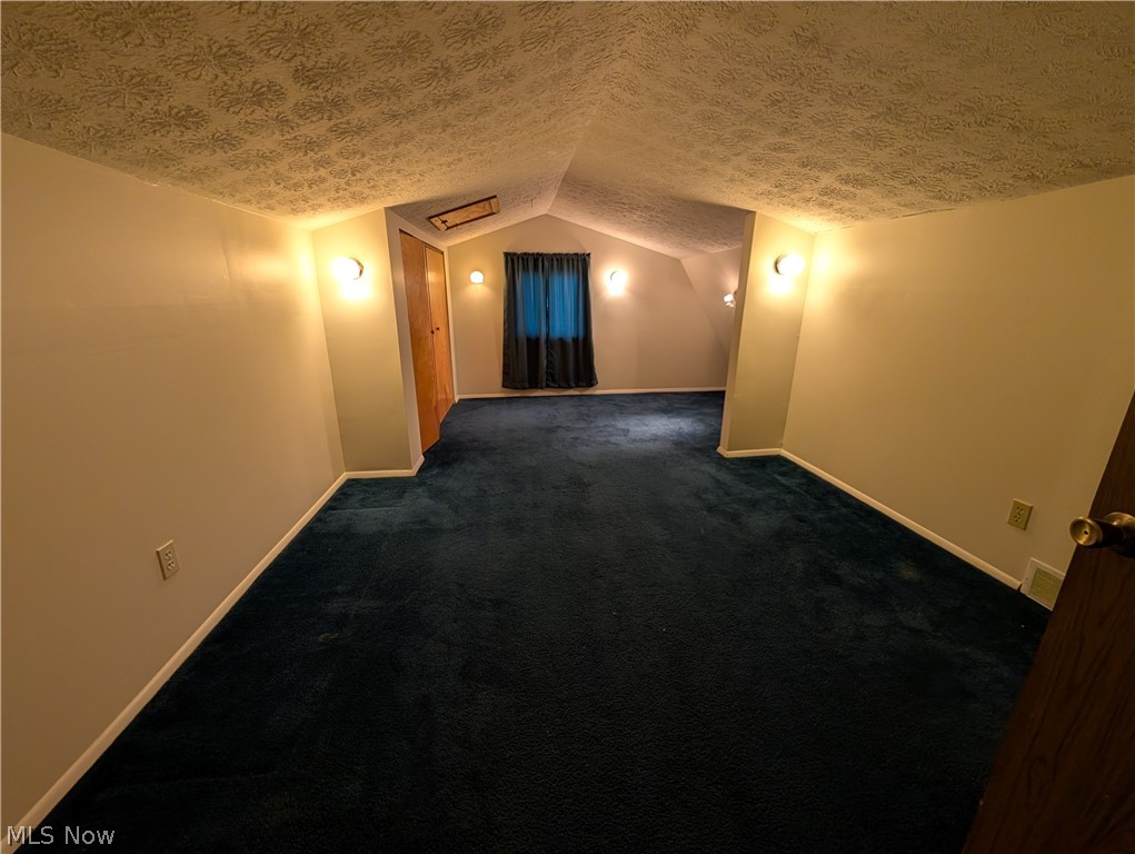5205 Blair Road Perry, OH 44081 - Photo 6 of 10 Spacious room featuring deep blue carpeting, sloped ceilings, and warm wall sconce lighting