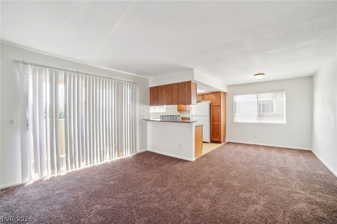 7200 West Pirates Cove Road, Unit 1049 Las Vegas, NV 89145 - Photo 11 of 12 Kitchen with open floor plan, a peninsula, light colored carpet, freestanding refrigerator, and wood finish cabinets