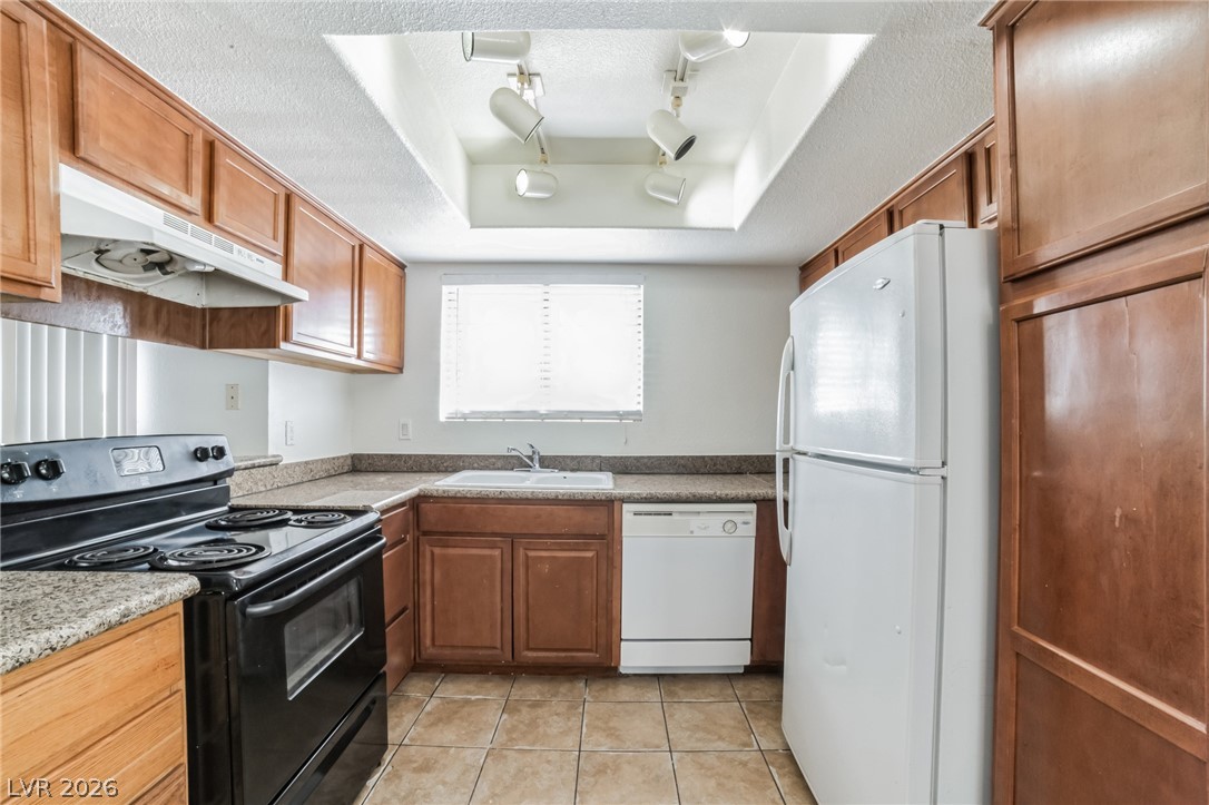 Kitchen with a textured ceiling, white appliances, light tile patterned floors, a tray ceiling, and wood finish cabinets