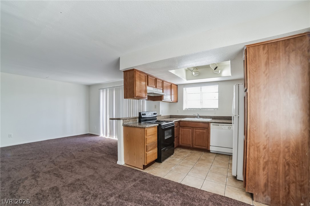7200 West Pirates Cove Road, Unit 1049 Las Vegas, NV 89145 - Photo 12 of 12 Kitchen featuring white appliances, light carpet, wood finish cabinets, light tile patterned flooring, and open floor plan