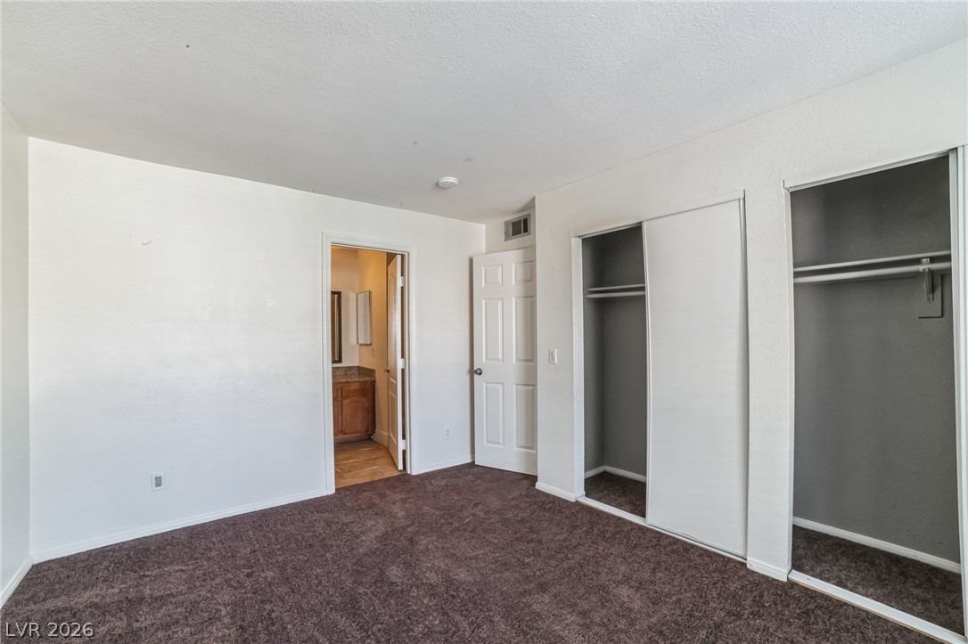 7200 West Pirates Cove Road, Unit 1049 Las Vegas, NV 89145 - Photo 7 of 12 Unfurnished bedroom with two closets, dark colored carpet, ensuite bath, and a textured ceiling