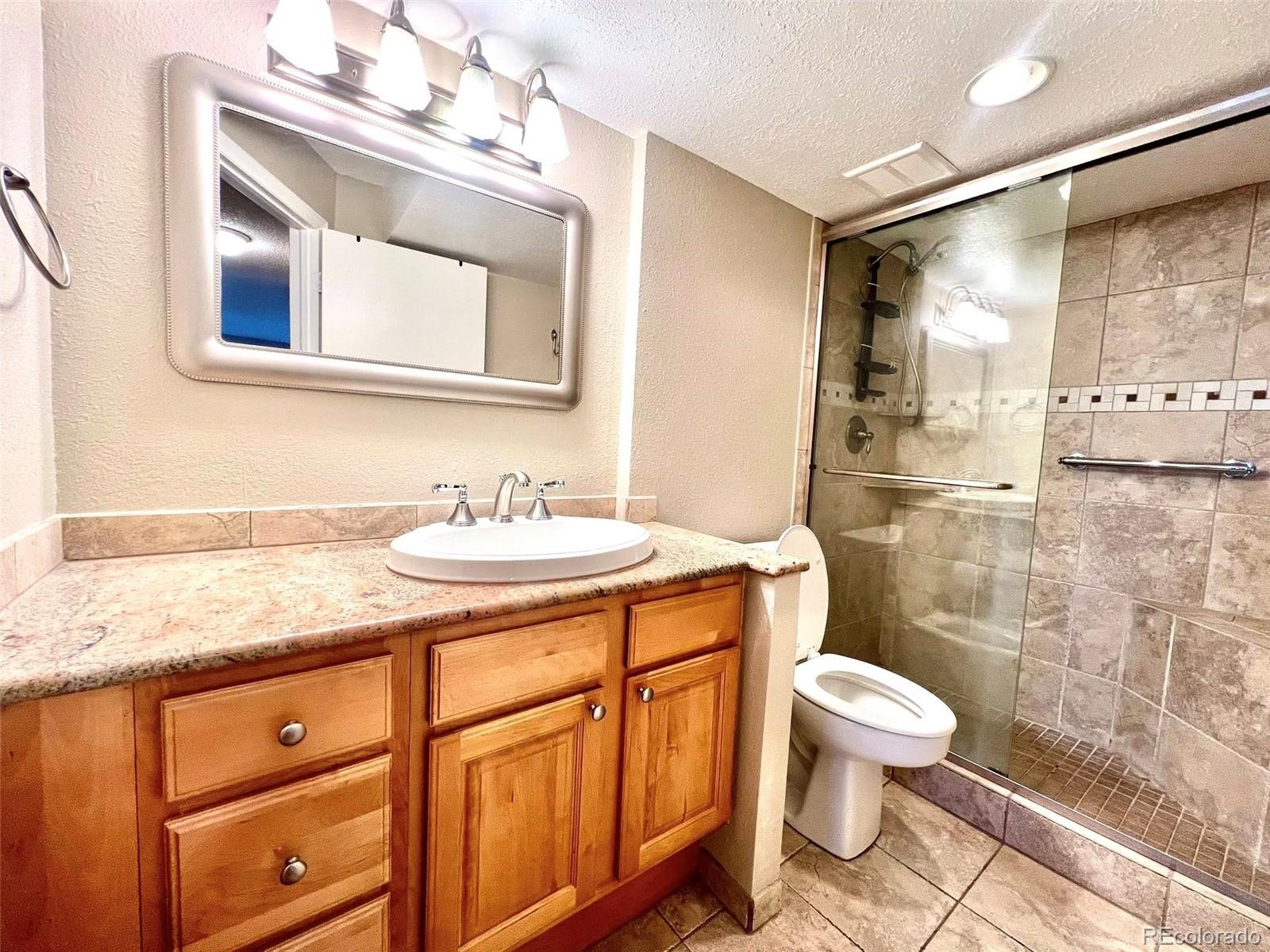 2 Adams Street, Unit 604 Denver, CO 80206 - Photo 15 of 41 a bathroom with a granite countertop sink a toilet a mirror and shower