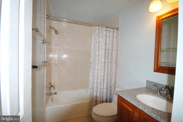 a bathroom with a granite countertop bathtub shower sink vanity and toilet