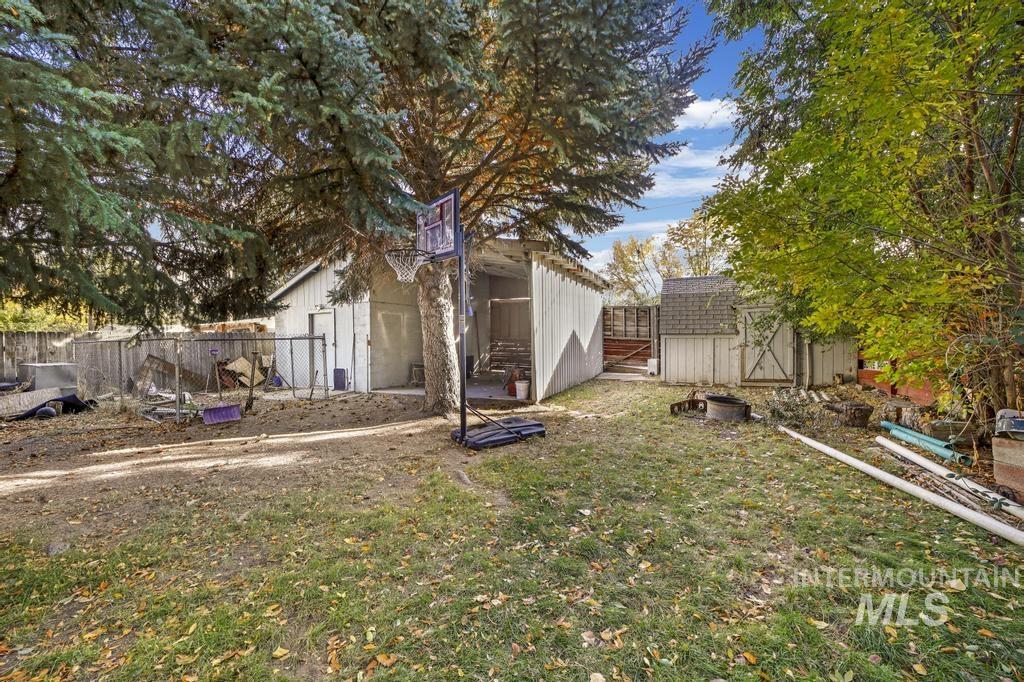 111 2nd Street Rupert, ID 83350 - Photo 9 of 45 Expansive backyard area featuring a large mature tree, a detached storage building with a shingled roof, a smaller storage shed with a shingled roof, and perimeter fencing