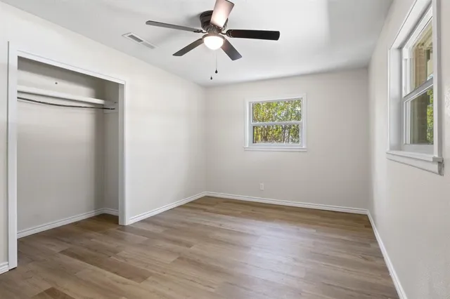 an empty room with wooden floor ceiling fan and windows