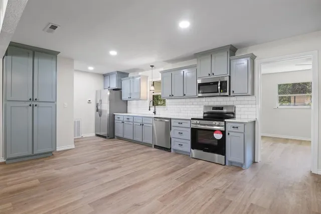 a kitchen with stainless steel appliances granite countertop a refrigerator a stove top oven a sink and dishwasher with wooden floor