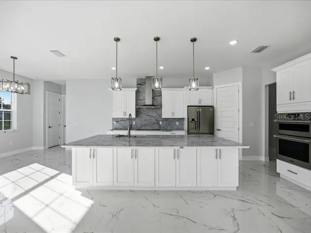 a large kitchen with kitchen island granite countertop a sink white cabinets and stainless steel appliances