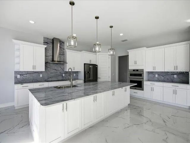a kitchen with stainless steel appliances granite countertop a sink a stove a oven a refrigerator and white cabinets