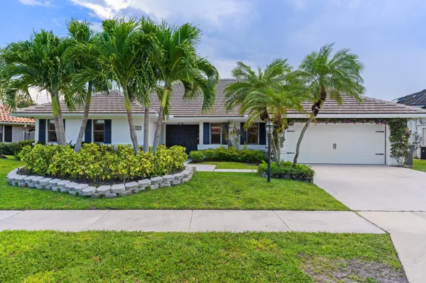 a front view of a house with a garden and palm trees