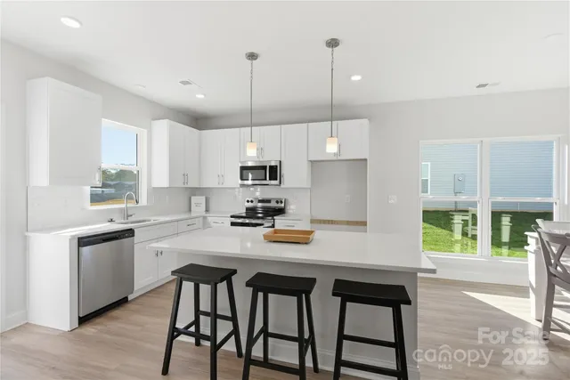 a kitchen with stainless steel appliances granite countertop a stove a refrigerator a sink a stove and white cabinets with wooden floor