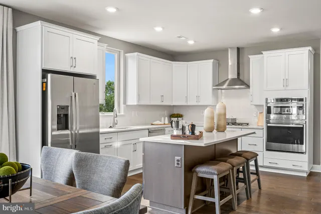 a kitchen with stainless steel appliances granite countertop a refrigerator a stove a sink a dining table and chairs with wooden floor