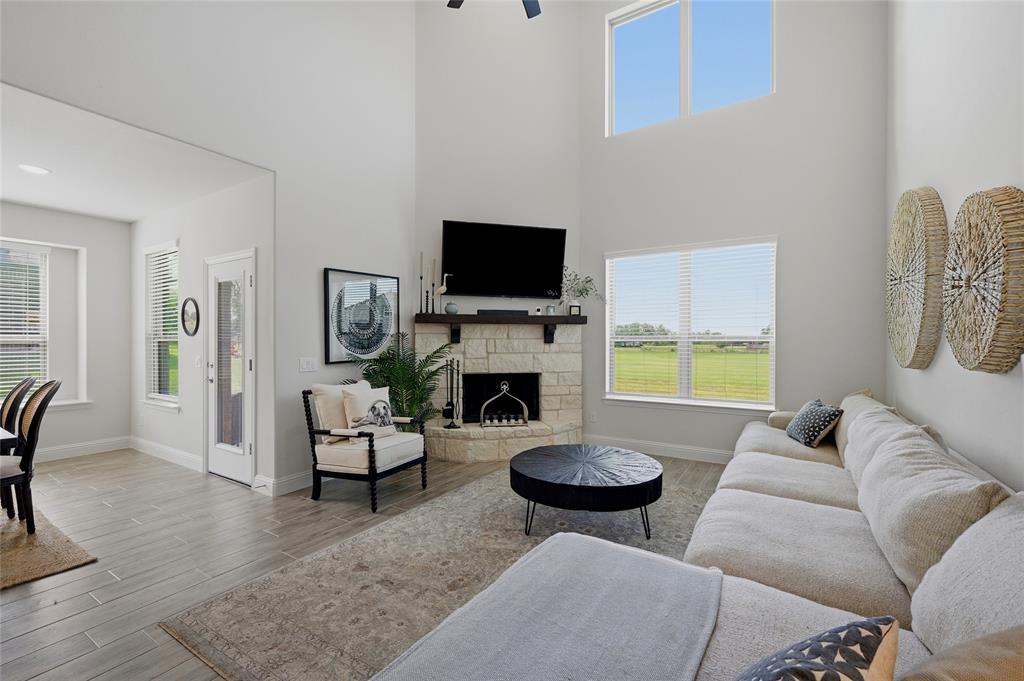 864 Shadow Valley Road Whitesboro, TX 76273 - Photo 20 of 40 Two-story living area featuring a stacked stone fireplace with a dark wood-finish mantel, high ceilings, large windows, and light wood-finish flooring