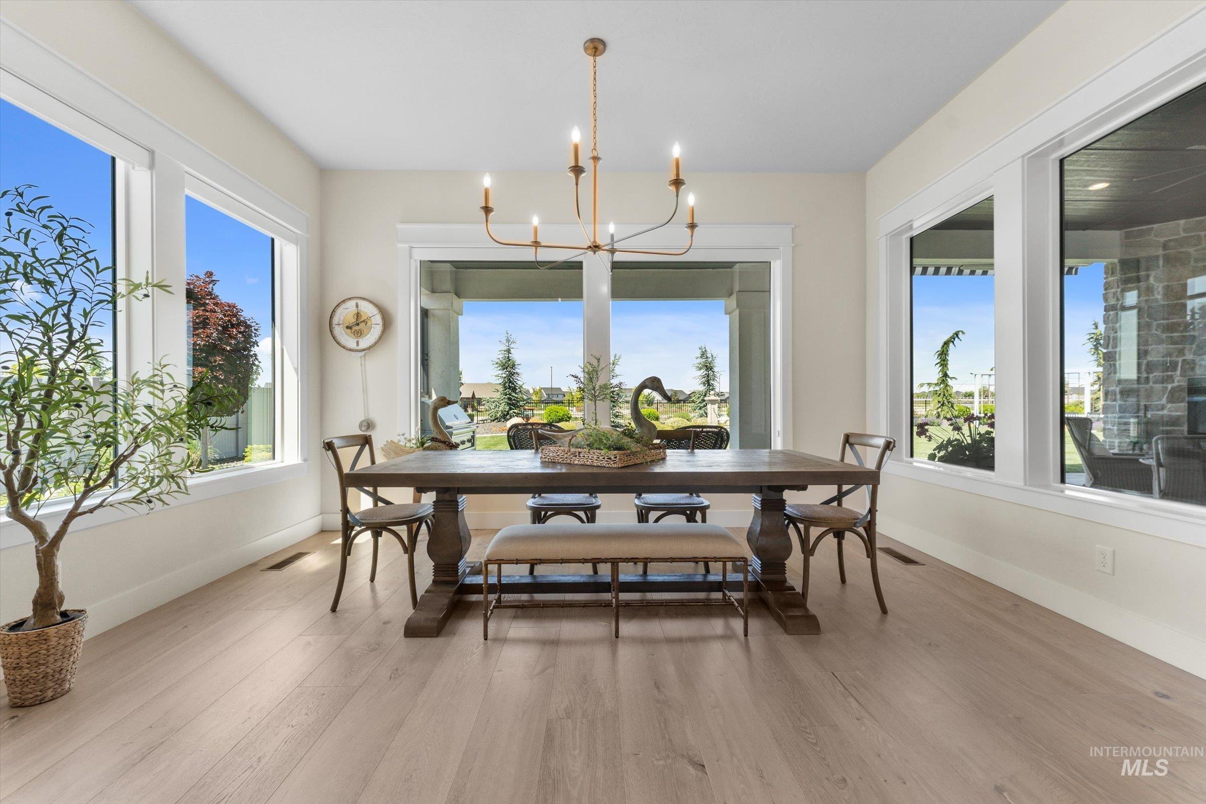 6585 South Pemberley Way Meridian, ID 83642 - Photo 10 of 43 Spacious dining area featuring expansive windows, wood-finish flooring, a contemporary chandelier, and direct access to an outdoor living space
