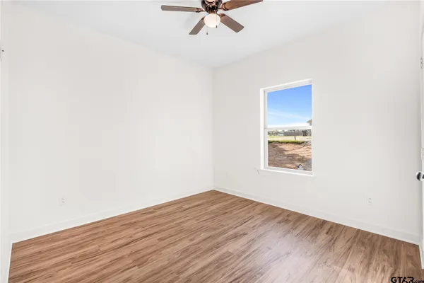 an empty room with wooden floor chandelier fan and windows