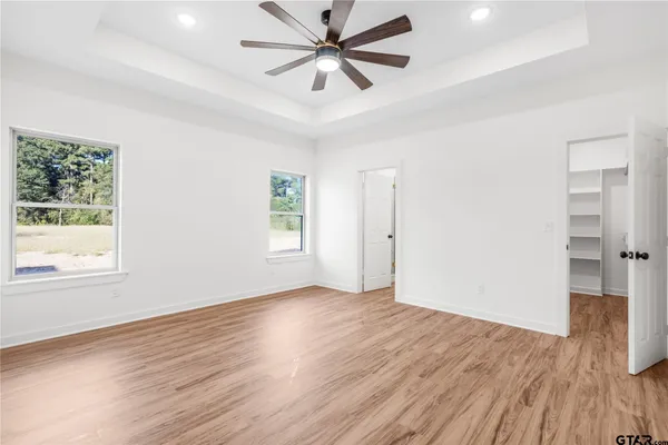 an empty room with wooden floor ceiling fan and windows