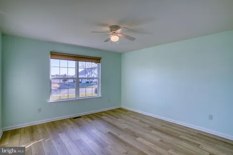 an empty room with wooden floor chandelier fan and windows