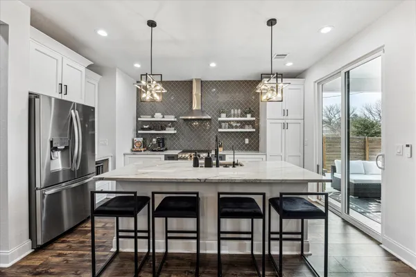 a kitchen with stainless steel appliances granite countertop a sink a refrigerator a stove a kitchen island with chairs and wooden floor