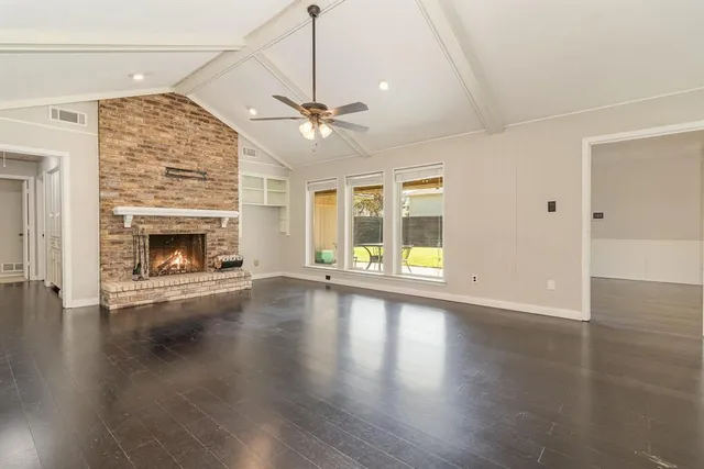 an empty room with wooden floor fireplace cabinet and windows