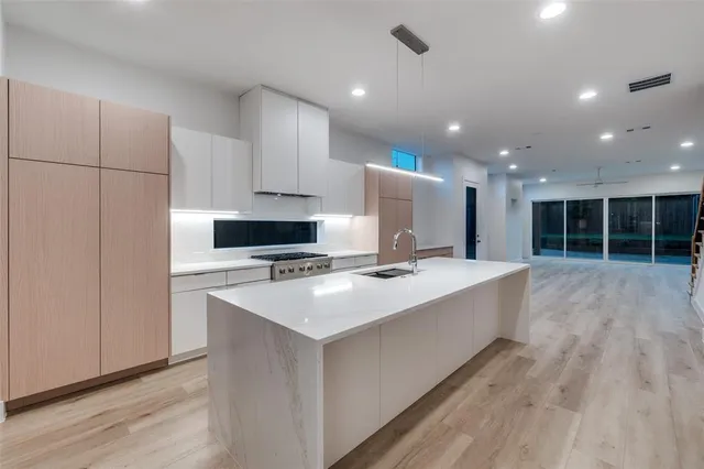 a large kitchen with kitchen island a stove a sink a refrigerator and white cabinets with wooden floor