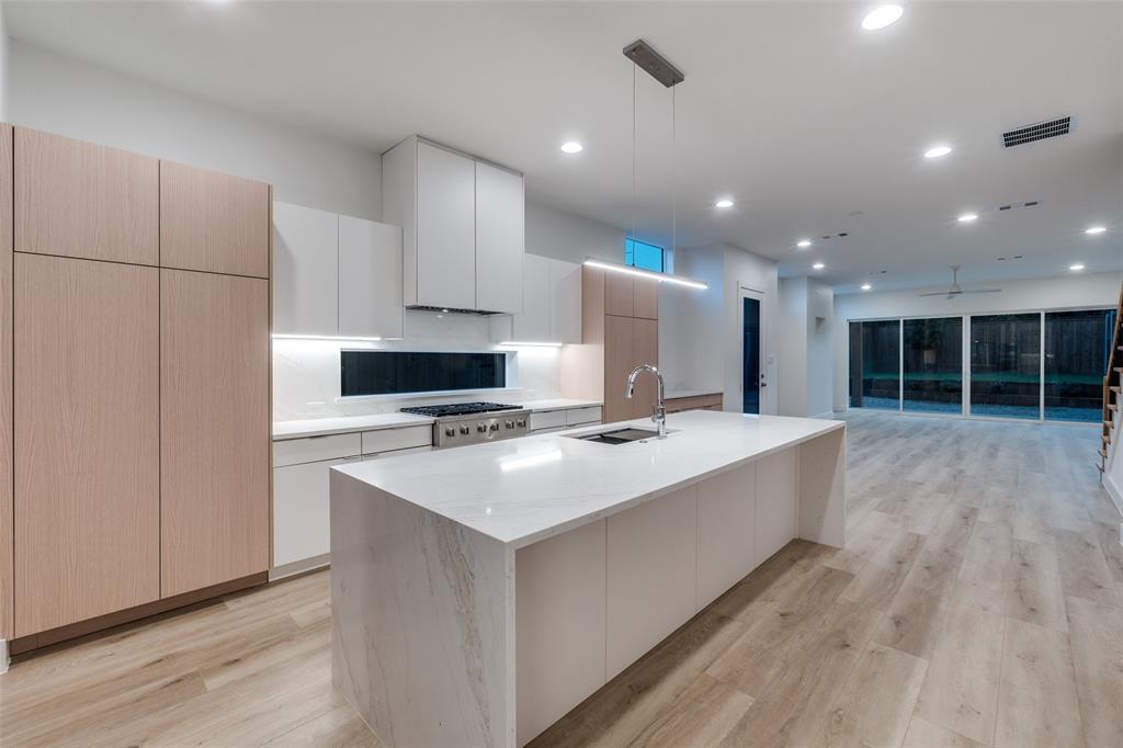 4515 Afton Street Dallas, TX 75219 - Photo 9 of 25 a large kitchen with kitchen island a stove a sink a refrigerator and white cabinets with wooden floor