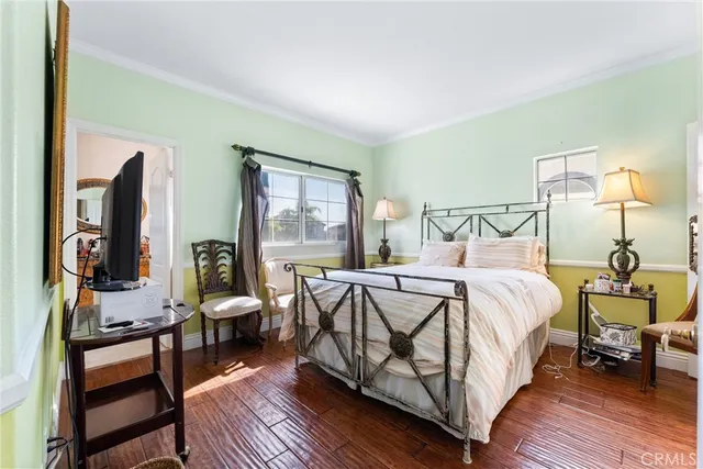 a bedroom with a bed a lamp on dresser and a wooden floor