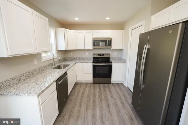 a kitchen with stainless steel appliances granite countertop a refrigerator a sink dishwasher a stove and white countertops with wooden floor