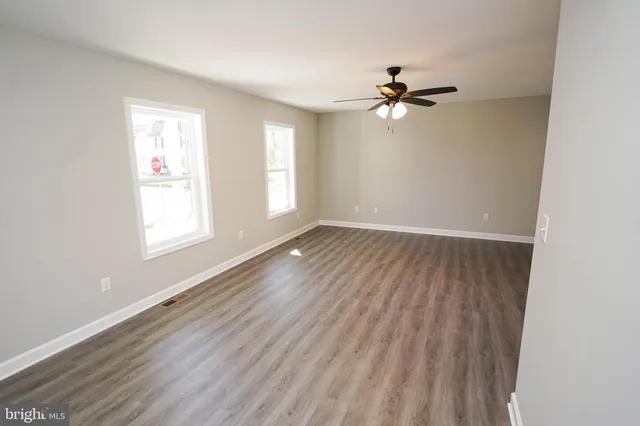 an empty room with wooden floor fan and windows