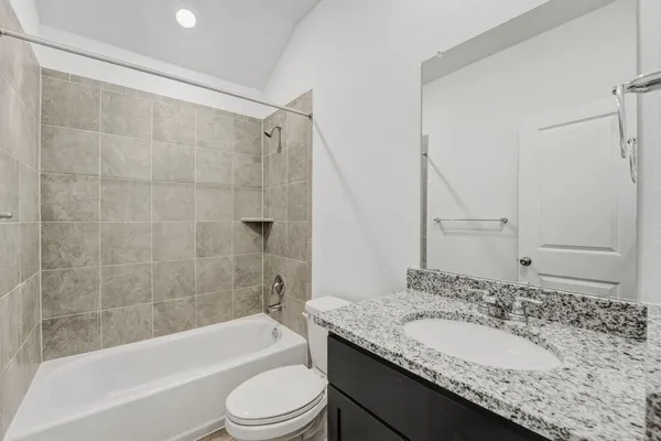 a bathroom with a granite countertop bathtub shower sink vanity and toilet