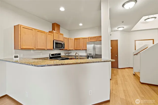 a kitchen with granite countertop a sink a stove top oven a refrigerator with wooden floors