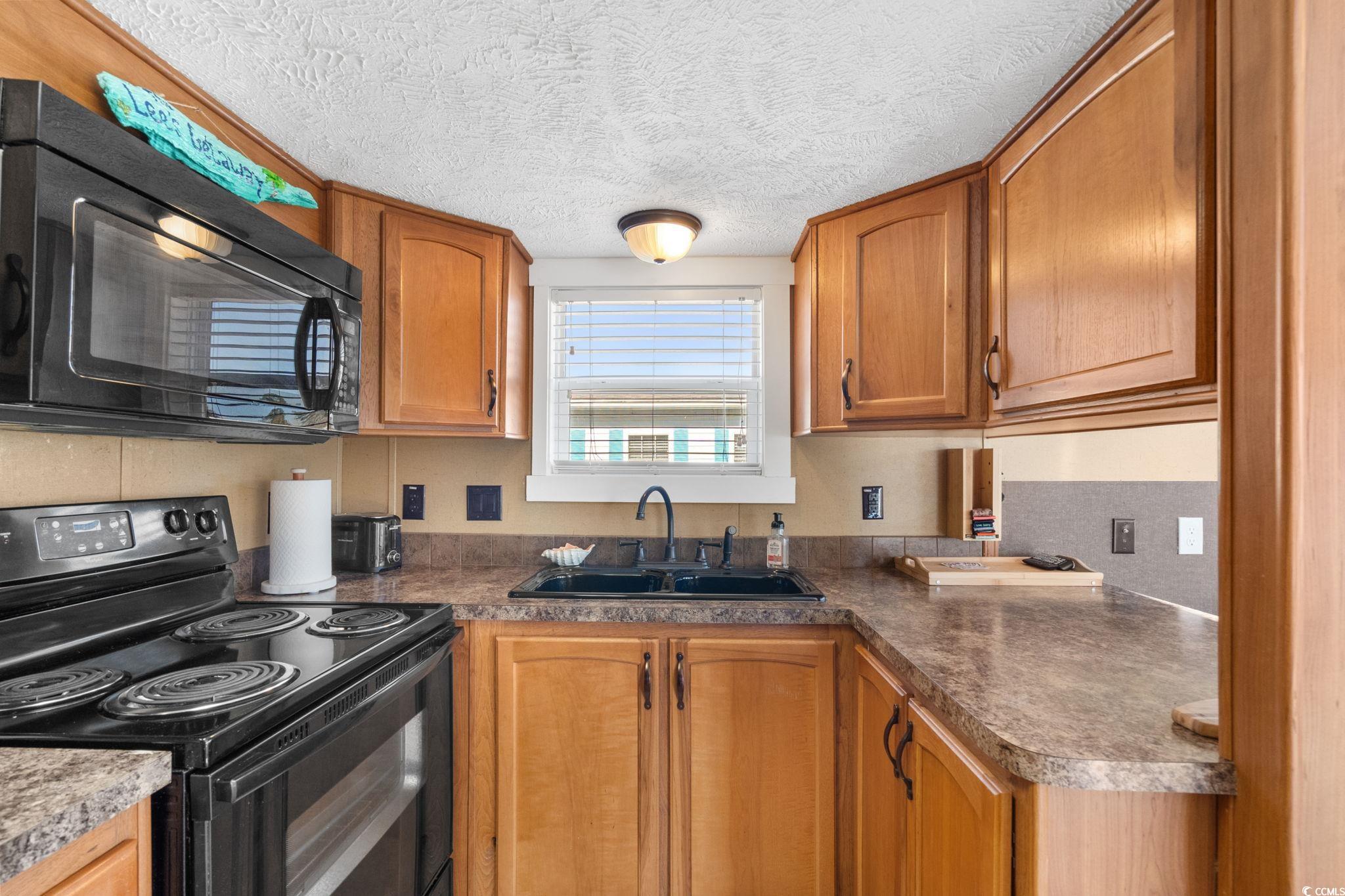 137 Riptide Circle North Myrtle Beach, SC 29582 - Photo 14 of 32 Kitchen with black appliances, a textured ceiling, brown cabinetry, and dark countertops