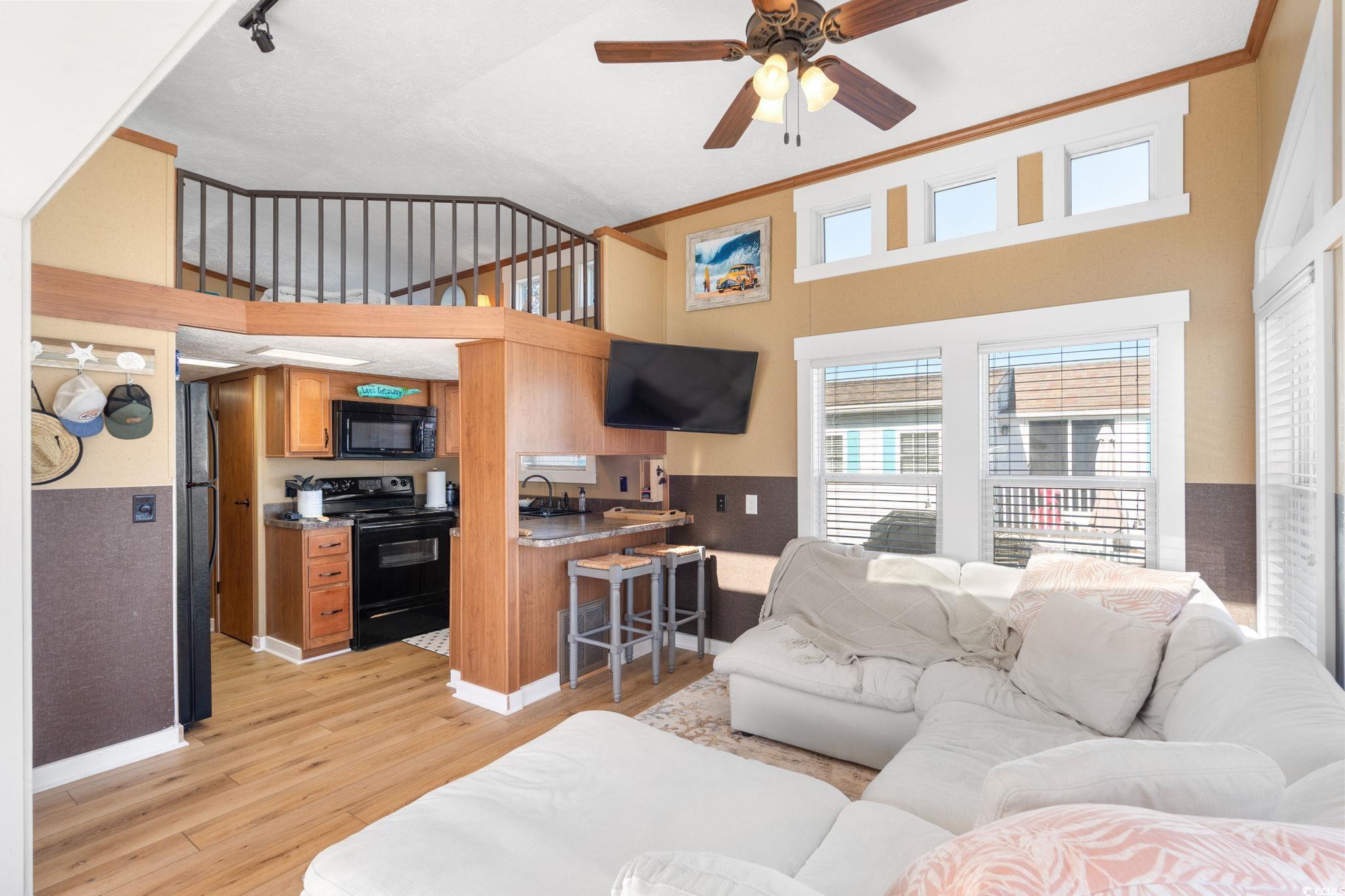 137 Riptide Circle North Myrtle Beach, SC 29582 - Photo 6 of 32 Living room featuring a towering ceiling, a ceiling fan, ornamental molding, light wood-style floors, and a wainscoted wall