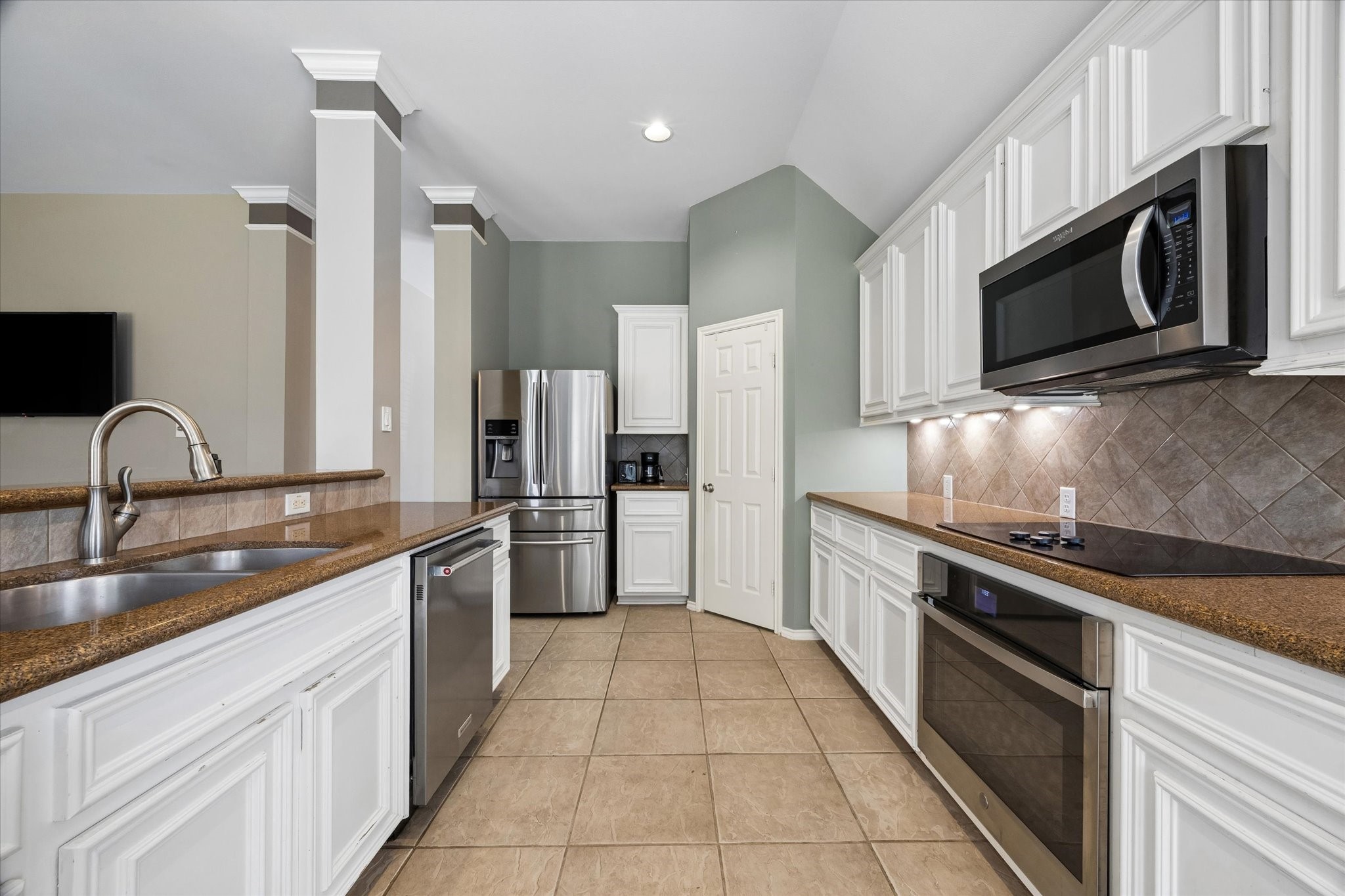 3118 Valley Court Manvel, TX 77578 - Photo 10 of 38 Modern kitchen with stainless steel appliances, white cabinetry, and ample counter space. Features a double sink, built-in microwave, and sleek electric cooktop, set against tiled backsplash and floor.