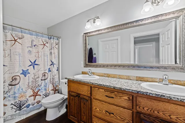 a bathroom with a granite countertop double vanity sink mirror and toilet