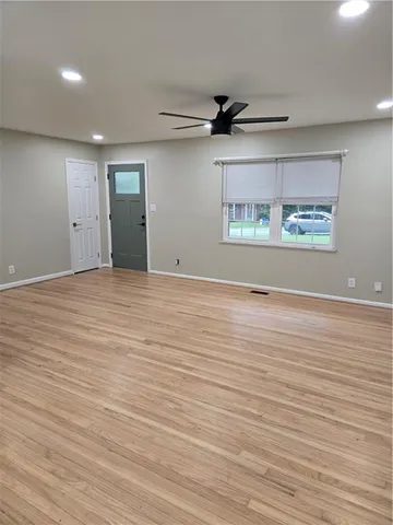an empty room with wooden floor ceiling fan and windows
