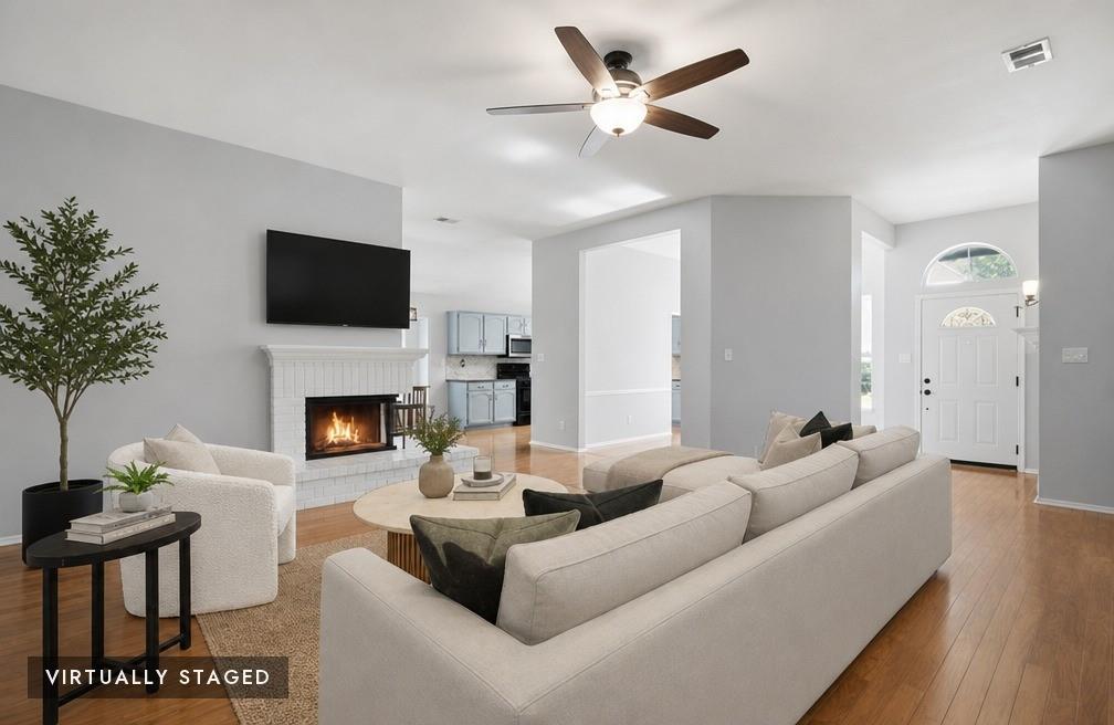 2074 Briarcliff Road Lewisville, TX 75067 - Photo 1 of 40 Living area featuring a white brick fireplace with hearth, wood-finish flooring, and a ceiling fan - Virtually staged
