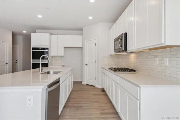 a large white kitchen with wooden floors stainless steel appliances and white cabinets