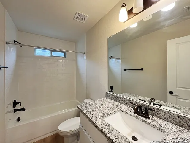 a bathroom with a granite countertop sink a toilet a mirror a bathtub and shower