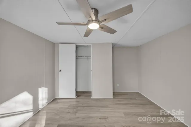 a view of an empty room with wooden floor and a ceiling fan