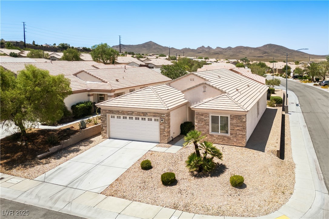2563 Sargon Street Henderson, NV 89044 - Photo 26 of 35 Ranch-style house featuring an attached garage, stone siding, a mountain view, concrete driveway, and stucco siding
