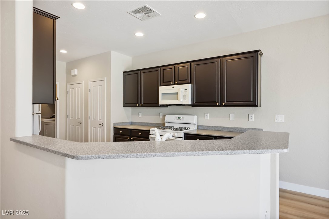 2563 Sargon Street Henderson, NV 89044 - Photo 10 of 35 Kitchen featuring white appliances, light countertops, dark brown cabinetry, recessed lighting, and a peninsula