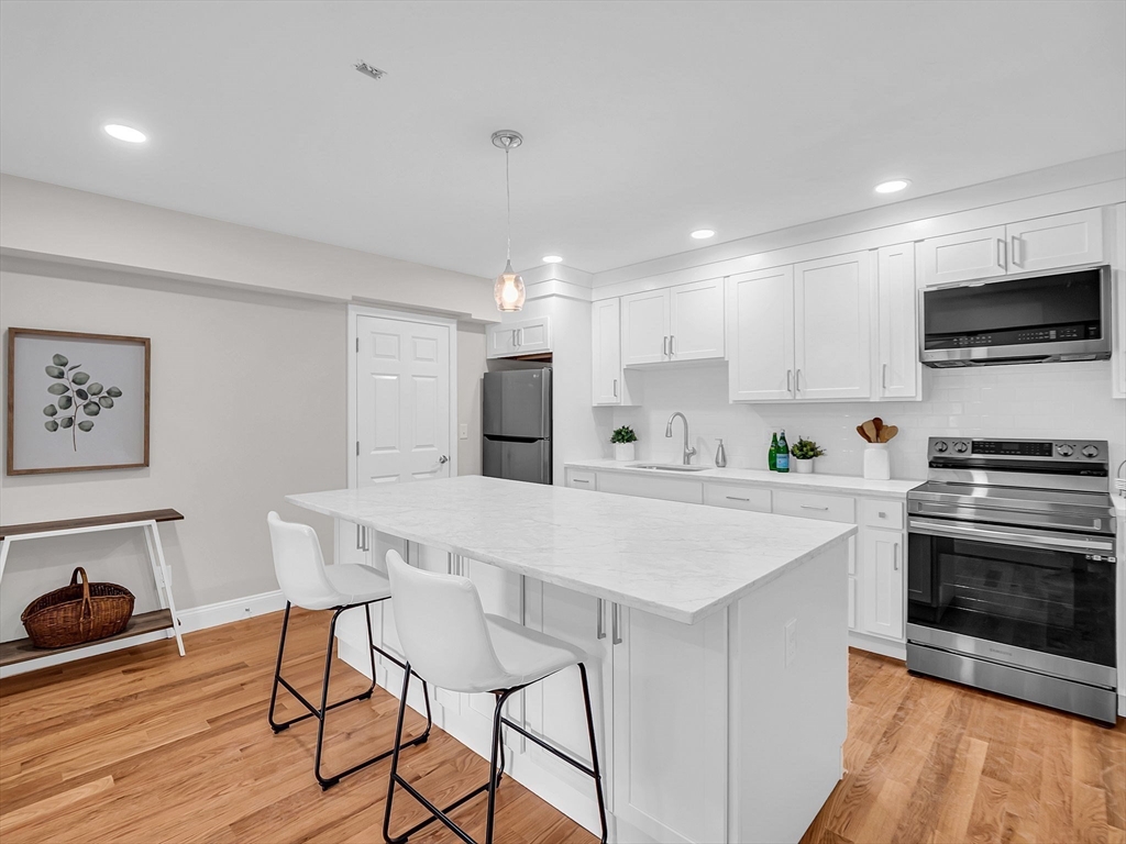 a kitchen with stainless steel appliances kitchen island granite countertop a stove a sink a microwave a dining table and chairs with wooden floor