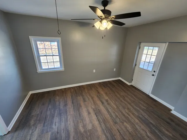 an empty room with wooden floor fan and windows