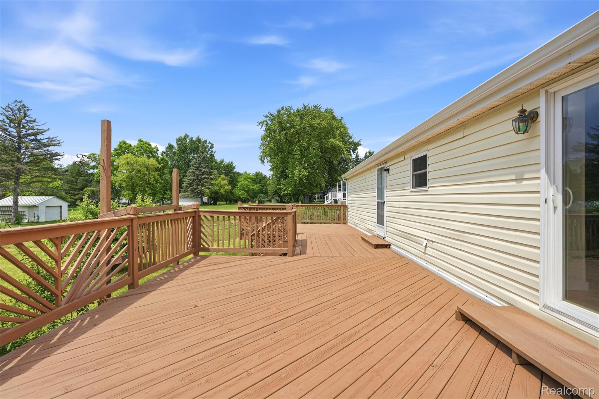 4420 Dublin Road Burton, MI 48529 - Photo 40 of 56 Expansive wood deck with a natural finish, featuring decorative railing, direct access to the interior via a sliding glass door, and a secondary entry door