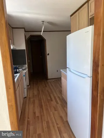 a view of a refrigerator in kitchen and an empty room with wooden floor