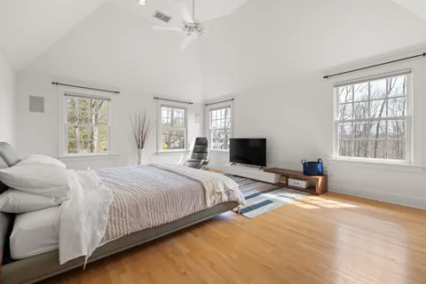 a bedroom with a bed a large window and wooden floor