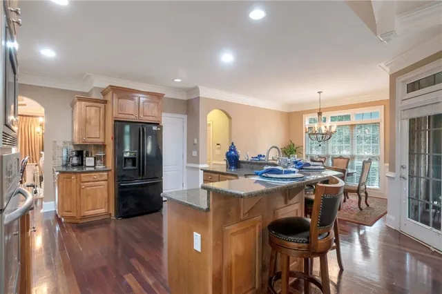 a kitchen with stainless steel appliances kitchen island granite countertop a stove a refrigerator a dining table and chairs with wooden floor