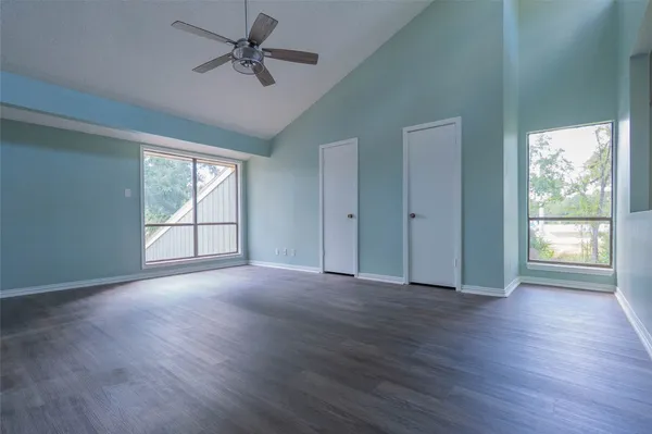 an empty room with wooden floor chandelier fan and windows