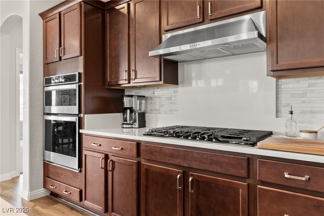 1221 Tortoise Ridge Mesquite, NV 89034 - Photo 24 of 56 Kitchen with backsplash, under cabinet range hood, stainless steel appliances, light wood-style flooring, and arched walkways