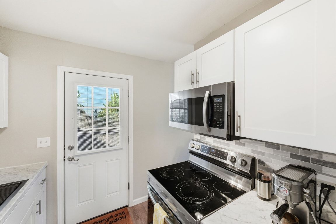 4615 Munson Street Austin, TX 78721 - Photo 14 of 27 Kitchen with appliances with stainless steel finishes, white cabinetry, backsplash, light stone countertops, and dark wood-style flooring